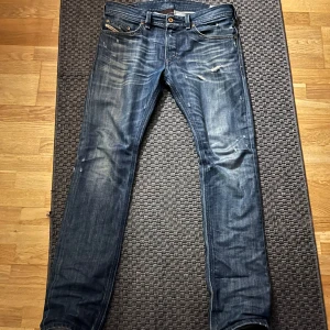 Blå jeans från Diesel - Snygga blå jeans från Diesel, modell Thavar. De har en slim-skinny passform och är tillverkade i denim med slitna detaljer för en cool look. Perfekta för en avslappnad stil.