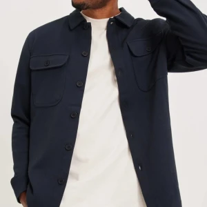 Mörkblå overshirt - Snygg mörkblå overshirt med knappar framtill och två bröstfickor med lock. Perfekt för lager-på-lager-stil. Långärmad design som passar bra till både vardag och mer avslappnade tillfällen.