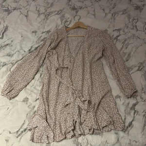 Blommig klänning från Bubbleroom - Säljer en söt blommig klänning från Bubbleroom i ljus beige med vita blommor. Klänningen har långa ärmar och volangdetaljer vid fållen. Perfekt för en romantisk look! 💐