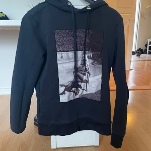 Svart hoodie från limitato - Snygg svart hoodie från limitatio med en unik tryckdetalj på framsidan. Tröjan har en klassisk huva med dragsko och långa ärmar. 