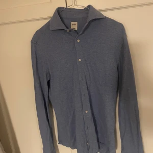 Blå skjorta från Boggi - Snygg blå skjorta från Boggi med klassisk krage och knappar framtill. Perfekt för en stilren look. Skjortan har långa ärmar och är tillverkad i ett mjukt material.1700kr nypris