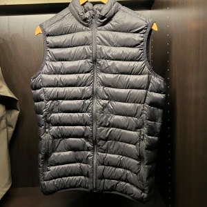 Svart dunväst från Everest  - Snygg och praktisk svart dunväst från Everest. Västen har en dragkedja framtill och är quiltad för extra värme. Perfekt för lager-på-lager under kyliga dagar.