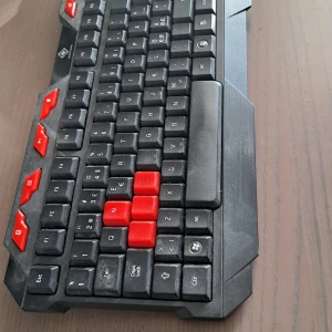 Svart och röd gamingtangentbord - Säljer ett coolt gamingtangentbord i svart med röda detaljer. Tangentbordet har en USB-anslutning och är designat för gaming med extra röda tangenter för WASD och piltangenter. Perfekt för den som vill ha en stilren och funktionell setup.