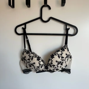 Vit och svart blommig Intimissimi BH  - Snygg bh i vitt med svart blommigt mönster och spetsdetaljer. Den har justerbara axelband med en mjuk push-up kupa och en elegant design som passar perfekt under alla kläder. 75C