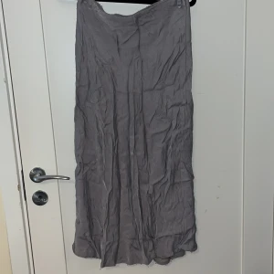 Grå långkjol från Kappahl - Säljer en elegant grå långkjol från Kappahl. Kjolen har en diskret dragkedja på sidan och är tillverkad i ett mjukt material som ger ett fint fall. Perfekt för en stilren look. Den är lite skrynklig men det är enkelt att stryka🩷