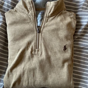 Beige tröja från Polo Ralph Lauren - Säljer en stilren beige tröja från Polo Ralph Lauren med halv dragkedja och broderad logotyp på bröstet. Perfekt för en avslappnad och snygg look. Tröjan har långa ärmar och är tillverkad i ett mjukt material. Använd typ en gång och pris går att diskutera vid ett snabbt köp!