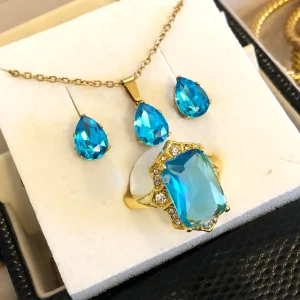 Smyckeset med turkos blå stenar guld  - Snyggt smyckeset i guld färg metall med ett halsband och örhängen Både halsbandet och örhängena har dropp formade blå turkos färgade stenar. Ringen är samma färg och stor cocktail modell med små vita kristaller runt mitten stenen. De är i jätte fint skick och bara använt på en fest förra året. Jag vet inte storlek på ring men gissar ca 17-17,5 jag har den på mitt mitten finger på vänster hand. 