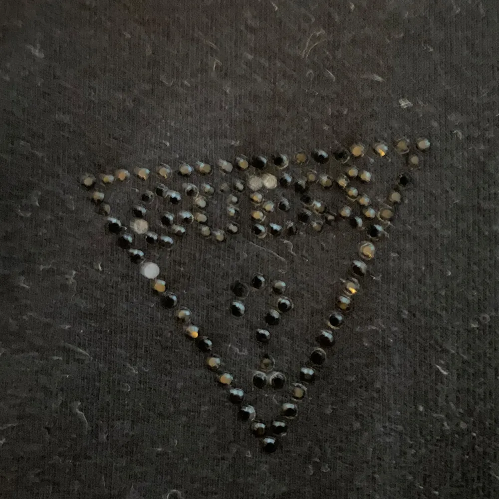 Säljer en stilren svart topp från Guess med korta ärmar och rund halsringning. Toppen har ett diskret Guess-logotyp i strass på bröstet. Perfekt för en enkel och snygg look.. Yläosat.