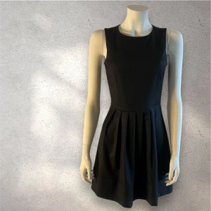 Svart ärmlös klänning - Elegant svart ärmlös klänning med rund hals och veckad kjol från Class. Perfekt för en stilren look. Made in Italy. Storlek: 38/ italy passar till 36