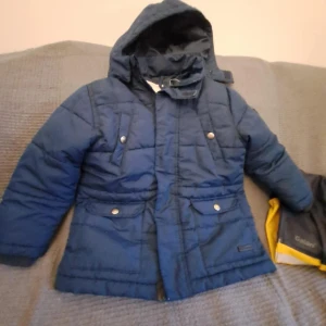 Blå quiltad jacka från KappAhl - Säljer en blå quiltad jacka från KappAhl med huva och dragkedja. Jackan har tryckknappar och praktiska fickor framtill. Perfekt för kyligare dagar.