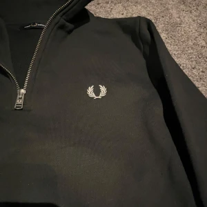 Mörkgrön hoodie från Fred Perry - Säljer en stilren mörkgrön hoodie från Fred Perry med dragkedja och det klassiska logotypbroderiet på bröstet. Tröjan har ribbade muddar och en bekväm passform. Perfekt för en avslappnad stil.🙌🏻