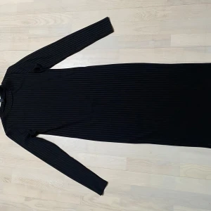 Svart ribbad klänning - Snygg svart ribbad klänning med lång ärm och figurnära passform. Perfekt för en stilren look. Strl M. 