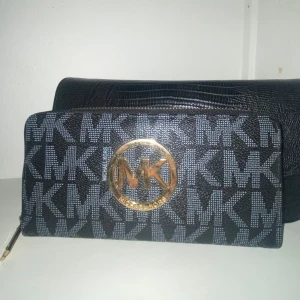 Grå/svart plånbok från Michael Kors - Säljer en plånbok/kuvertväska från Michael Kors. Knappt använd så väldigt bra skick. Plånboken har flera fack för kort och en dragkedja för mynt. 