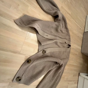 Beige stickad kofta från H&M - Säljer en mysig beige stickad kofta från H&M. Koftan har stora knappar framtill och en ribbad struktur som ger en stilren look. Perfekt för kyliga dagar. Passar bra till både jeans och kjol. 🧥✨(Priset kan diskuteras💕)