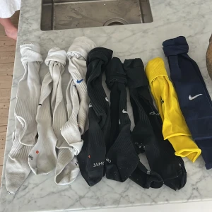 Fotbollsstrumpor från Nike och Adidas. - Säljer ett gäng strumpor från Nike och Adidas i olika färger. Det finns vita (Nike), svarta (Nike), gula (adidas) och blå strumpor (Nike) med den klassiska Nike-loggan. Perfekta för dig som spelar fotboll. De svarta och vita strumporna  är långa och har en ribbad design för extra komfort. De blåa är sleeves alltså har de ingen strumpa, utan man ska ha tex grepp strumpor under. De gula är från adidas och är också sleeves. Pris: 150 kr för alla  Nypris: 150kr per par.