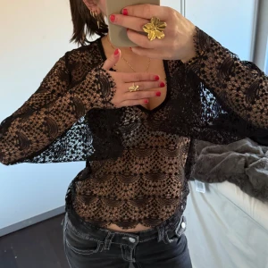 Svart spetsblus - Snygg svart spetsblus med v-ringning och långa ärmar. Blusen har ett detaljerat spetsmönster som ger en elegant look. Perfekt för att lägga till en touch av stil till din outfit.