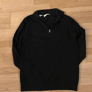 Svart tröja med dragkedja - Snygg svart tröja med dragkedja vid halsen. Perfekt för en stilren look och passar bra till jeans. Tröjan har långa ärmar och en normal passform.