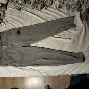 Grå mjukisbyxor från Champion - Säljer ett par grå mjukisbyxor från Champion i storlek XL. Byxorna har snörning i midjan och ett broderat Champion-märke på benet. Perfekta för en avslappnad stil. Ena sidan av snöret saknar plastgrejen (se bild).