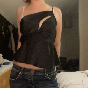 Svart topp - Svart topp med asymmetrisk design och volangdetaljer.