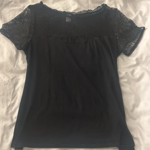 Svart spetsdetaljerad topp från H&M - Snygg svart topp från H&M med spetsdetaljer på ärmarna och upptill. Storlek L, men passar som M. Perfekt för en elegant look. Toppen har korta ärmar och en rund halsringning.