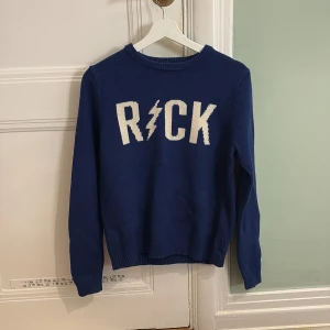 Blå stickad tröja från Zadig & Voltaire - Snygg blå stickad tröja från Zadig & Voltaire med texten 'ROCK' i vitt på framsidan. Tröjan har långa ärmar och en rund halsringning. Perfekt för en cool och avslappnad stil. Det står ingen storlek men skulle säga S.