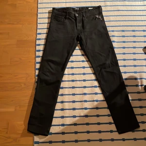 Svarta jeans från Replay - Snygga svarta jeans från Replay, modell Anbass. De har en klassisk femficksdesign med dragkedja och knapp. Perfekta för en stilren look. Också en liten slitning där bak som enkelt går att fixa