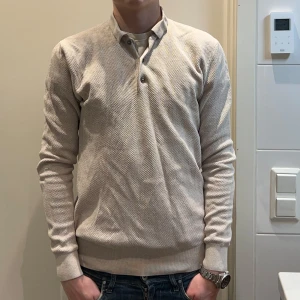 Beige pikétröja från Bläck - Snygg beige långärmad pikétröja från Bläck med krage och knappar framtill. Tröjan har en mycket snygg textur. Han på bilden är 183 cm 70 kg. nypris 699! ända defekt är ett pytte litet håll i armhålan 