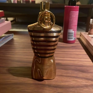 Guldglänsande parfymflaska - Elegant parfymflaska i guld med en unik, ribbad design och en rund detalj på toppen. Flaskan har en lyxig och modern känsla, perfekt för den som vill ha något extra på sminkbordet.