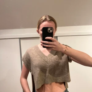 Beige stickad croppad topp - Säljer en beige stickad croppad topp med v-ringning. Perfekt för lager-på-lager eller sommarens varma dagar. Enkel och stilren design som passar till det mesta.