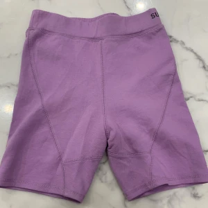 Lila shorts från Superdry - Säljer ett par lila shorts från Superdry. De har en elastisk midja och en diskret logga på sidan. Perfekta för en avslappnad stil.