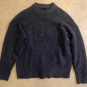 Mörkblå stickad tröja från 157 - Mysig mörkblå stickad tröja från 157. Perfekt för kyliga dagar med sin mjuka och varma textur. Tröjan har långa ärmar och en klassisk passform som passar till det mesta. Ett måste i garderoben för höst och vinter!