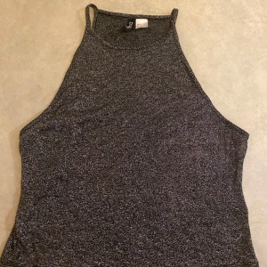 Glittrig linne från H&M Divided - Snygg glittrig linne från H&M Divided i en mörkgrå nyans. Perfekt för en kväll ute eller en festlig tillställning. Linnet har smala axelband och en hög halsringning.