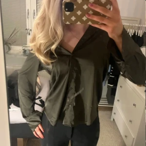 Olivgrön blus - Snygg olivgrön blus med knappar framtill. Blusen har en v-ringad design och långa ärmar, perfekt för en stilren look.