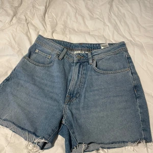 Blå jeansshorts från Yoke - Snygga blå jeansshorts från Yoke med fransiga kanter och klassisk femficksdesign. Perfekta för en avslappnad stil. De har en knappgylf och bälteshällor för extra stil och funktion.