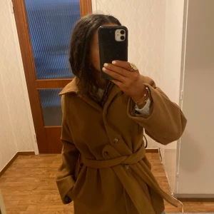 Brun kappa från Gina Tricot - Säljer en stilren brun kappa från Gina Tricot i storlek S. Kappan har en klassisk design med knappar och ett knytskärp i midjan för en elegant look. Perfekt för höst och vår. Lite nopprig. Priset är diskuterbart🥰🥰
