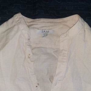 Vit skjorta från Smog - Säljer en stilren vit skjorta från Smog med knappar framtill. Skjortan har en avslappnad passform och är tillverkad i ett lätt material, perfekt för varmare dagar.