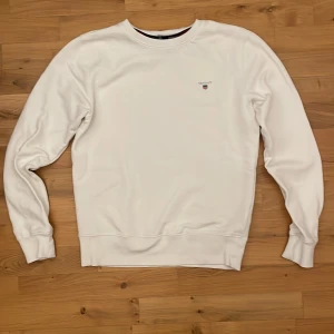 Vit sweatshirt från GANT storlek: S - Säljer en stilren vit sweatshirt från GANT med broderad logotyp på bröstet. Tröjan har långa ärmar och ribbade muddar vid ärmslut och nederkant. Perfekt för en avslappnad stil. Storlek:S. Skick: 10/10
