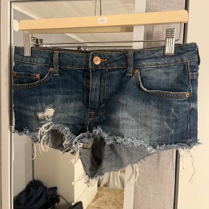 Blå lågmidjade jeansshorts - Jätte snygga lågmidjade jeansshorts från Gina tricot, shortsen är köpte second hand och slutade säljas för länge sen. Passar S/XS/XXS. Perfekt till sommaren och trendiga.