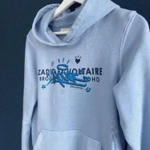 Ljusblå hoodie från Zadig & Voltaire - Snygg ljusblå hoodie från Zadig & Voltaire med tryck i svart och blått på bröstet. Perfekt för en avslappnad stil. Fråga om mer frågor 🥰🥰köpt på NK barnavdelning