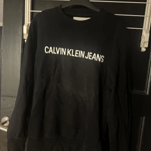 Svart tröja från Calvin Klein Jeans - Snygg svart tröja från Calvin Klein Jeans med vit logga på framsidan. Perfekt för en stilren och avslappnad look. Tröjan har långa ärmar och en klassisk rund halsringning.