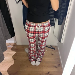 Rutig pyjamasbyxa i rött och vitt - Mysiga pyjamasbyxor med rött, vitt och svart rutmönster. Byxorna har en avslappnad passform och elastisk midja för extra komfort. Perfekta för en lugn hemmakväll.