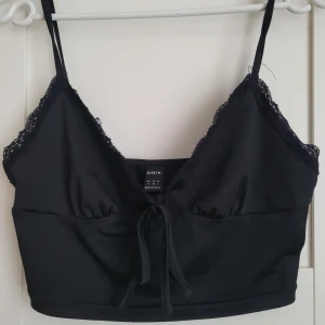 Svart linnetopp från Shein - Snygg svart linnetopp från Shein med spetsdetaljer och knytning framtill. Perfekt för en stilren look. Tillverkad i ett mjukt material med smala axelband.