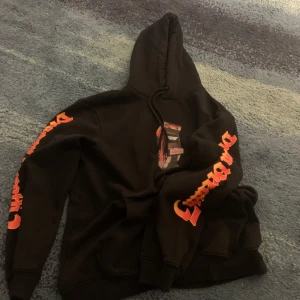 Svart hoodie med tryck - Snygg svart hoodie med orange tryck på ärmarna och bröstet. Perfekt för en avslappnad stil med en skön passform och huva.