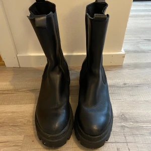 Svarta boots från Tamaris - Snygga svarta boots från Tamaris i skinn med grov sula. Perfekta för höst och vinter med en stilren design och praktiska dragflikar för enkel påtagning. Skorna är använda max 5 gånger förlängden är 23.8 nypris är 1400kr