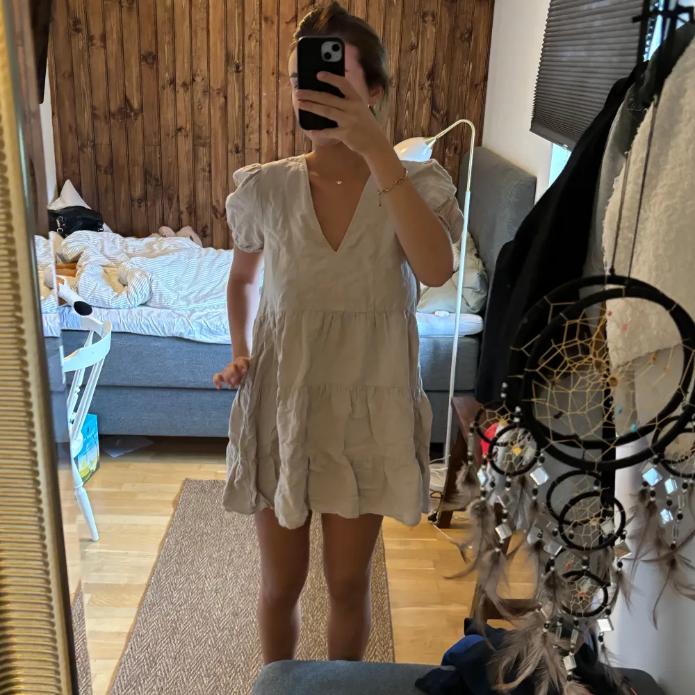 Säljer en superfin beige kortklänning med volangdetaljer. Den har en v-ringad hals och korta ärmar som ger en söt och somrig look. Perfekt för en avslappnad dag eller en sommarfest! 💛. Klänningar.