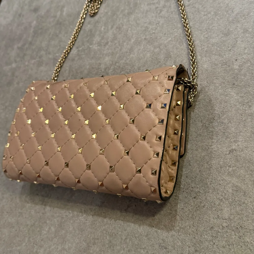 Jag säljer min otroligt fina ROCKSTUD SPIKE NAPPA LEATHER CROSSBODY CLUTCH BAG i färgen Poudre. Väskan är i mycket bra skick.🩷 Ny pris 20 975kr. Pris går att diskutera. Skriv för fler bilder🫶🏽. Väskor.