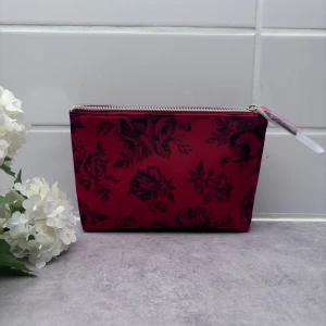 Röd necessär från Victoria's Secret - Säljer en superfin röd necessär från Victoria's Secret med ett vackert blommigt mönster. Den har en praktisk dragkedja och insidan är randig i matchande färger. Perfekt för att förvara smink eller andra småsaker!