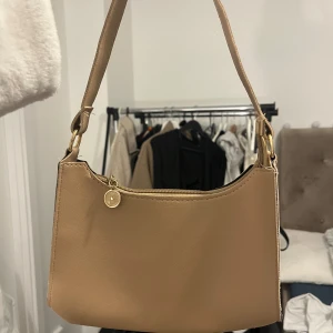 Beige/brun handväska  - Beige/brun liten handväska med guld detaljer. Säljer för 15kr 