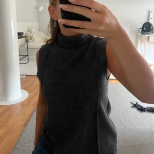 Mörkgrå ärmlös polotröja - Säljer en stilren och mysig mörkgrå ärmlös polotröja. Perfekt för lager-på-lager under hösten eller vintern. Tröjan är stickad och har en hög polokrage som håller dig varm. Passar både till jeans och kjol för en avslappnad men chic look. Den formar kroppen jättefint!