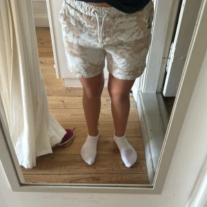 Beige camouflagemönstrade shorts - Säljer ett par bekväma och stiliga shorts i beige camouflagemönster. De har en avslappnad passform med resår och snörning i midjan för extra komfort. Perfekta för en avslappnad dag eller sommaräventyr!